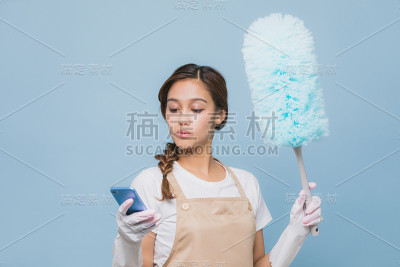 年轻女子一边看智能手机一边打扫房间。