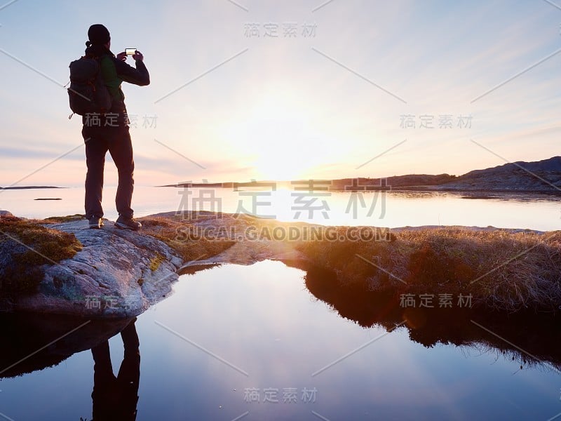 旅行男子在海上拍照的背影剪影。游客背着背包站在岩石上