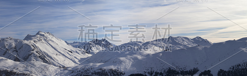 冬季高山上的雪坡全景和晚上蓝色阳光下多云的天空