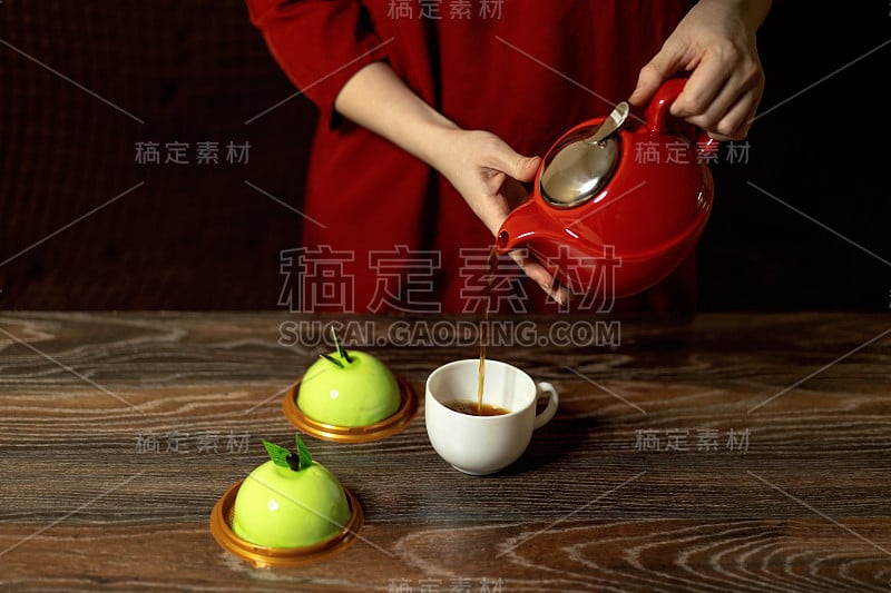 红裙背景上的女性双手将茶从红茶壶倒入白杯子。