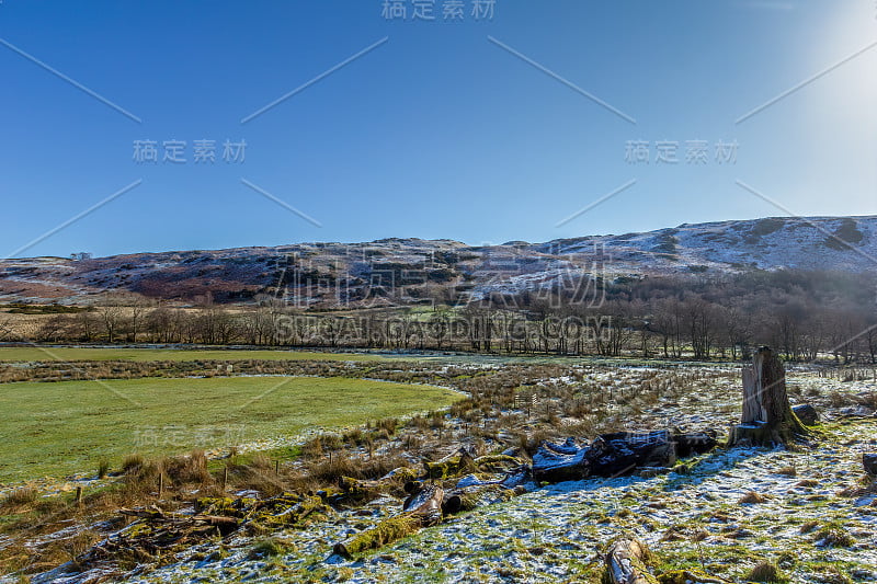 这是一个美丽的乡村景色，雪绿的田野和山脉斜坡在雄伟的蓝天下的背景