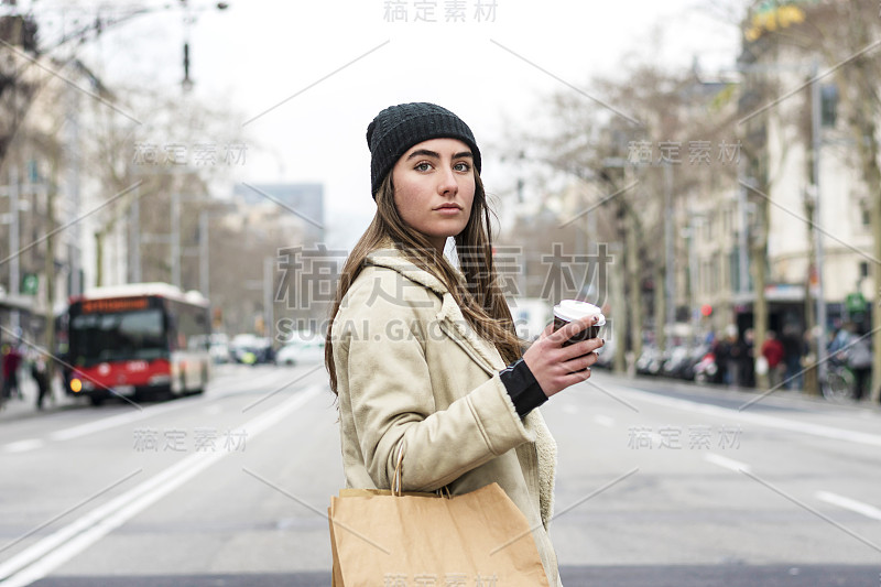 一名年轻的欧洲女子走在城市街道上，手里拿着外卖的咖啡