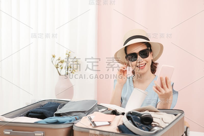 漂亮的女人旅行者拍摄自拍和选择时尚的帽子准备打包衣服到手提箱度假在家