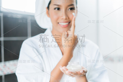 亚洲女性在浴室沐浴后将面霜和乳液涂在脸上。