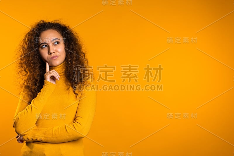 在黄色背景下，思考的女人抬头环顾四周。忧虑沉思的表情。漂亮的卷发女孩模特