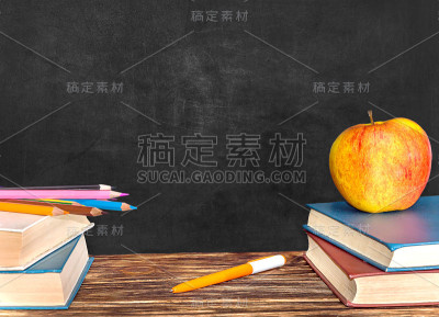 书，彩色铅笔，钢笔和苹果在黑板的背景