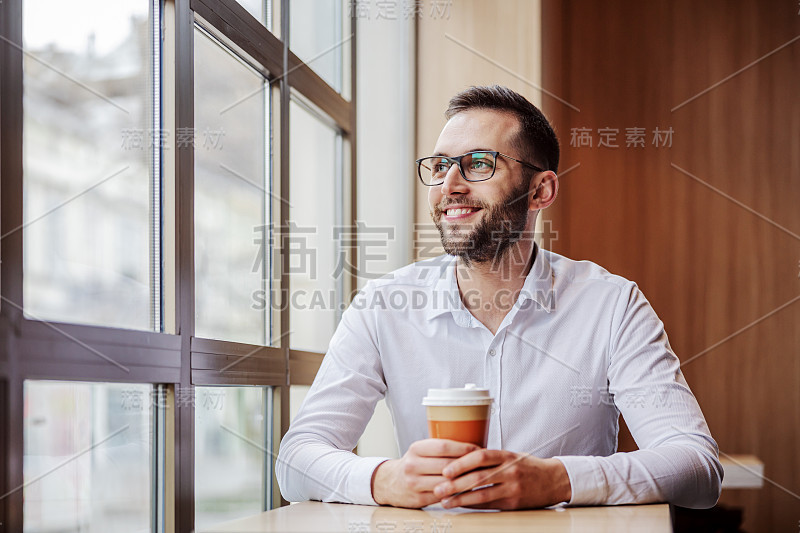 年轻男子微笑优雅地坐在快餐店里，拿着一次性咖啡杯，看着槽窗。他正在吃午饭。