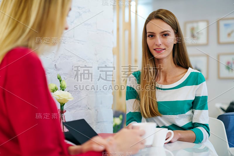 肖像漂亮的年轻女子在休闲穿着看着相机，与同事在休息期间交谈，美丽的女性享受友好的会议在舒适的咖啡馆休