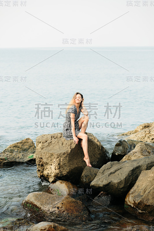 一个年轻美丽的女孩穿着大石头，风景如画的海边