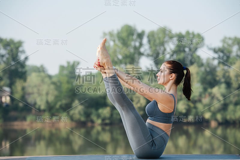 在河边的一个美丽的地方做瑜伽的年轻女子的侧视图