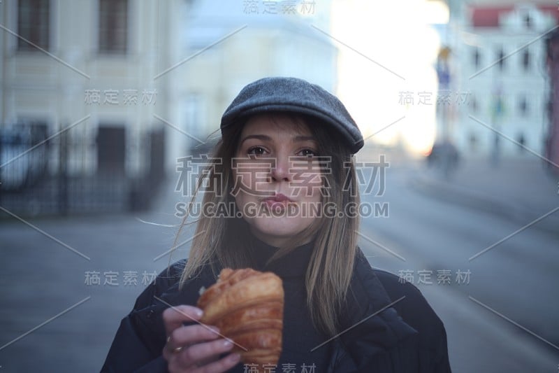 年轻漂亮的女孩在街上吃牛角面包