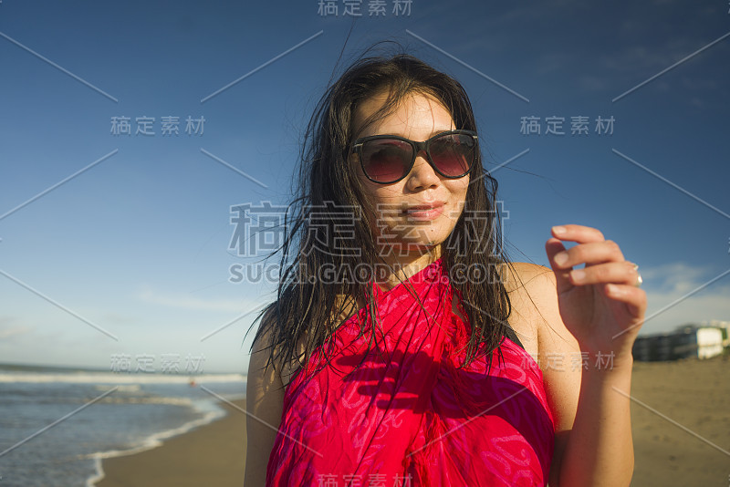 户外生活方式的肖像，年轻美丽和快乐的亚洲华人妇女穿着纱笼和太阳镜在海滩上散步的海边，放松的微笑，愉快