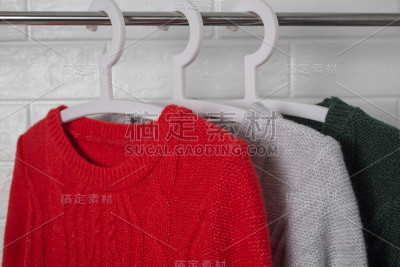 衣服挂在衣架上。红、绿、杂色的毛衣。时尚和风格，展示，商店，概念。白色砖墙，舒适和清洁，设计，舒适，
