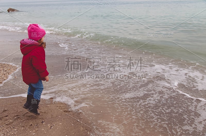 穿着红夹克的小女孩在海滩上玩海浪