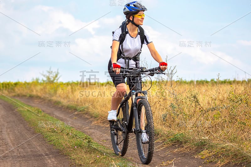 骑自行车的漂亮女孩骑着自行车在田野上。健康的生活方式和运动。业余爱好