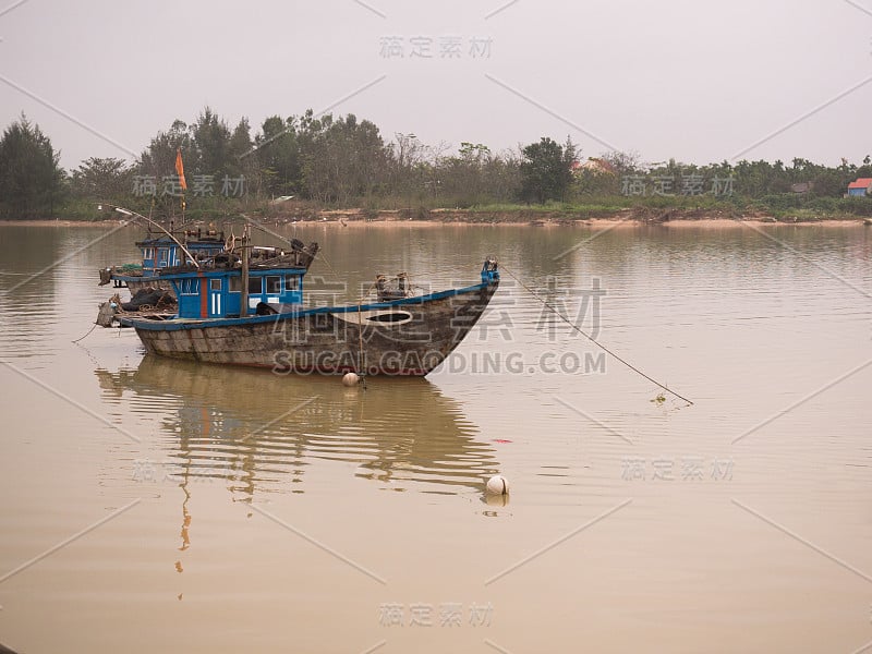 越南传统的海上捕鱼木船，背景是一条黄河，岸边是会安河的树木