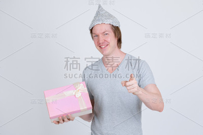 快乐的年轻人拿着锡纸帽，拿着礼盒，指着相机