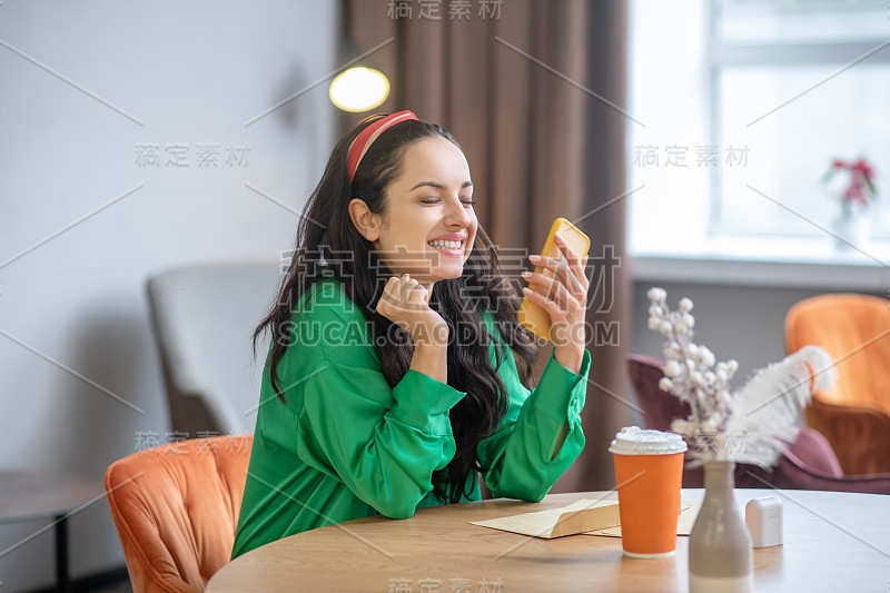 身着祖母绿衬衫的快乐女人，手里拿着智能手机。