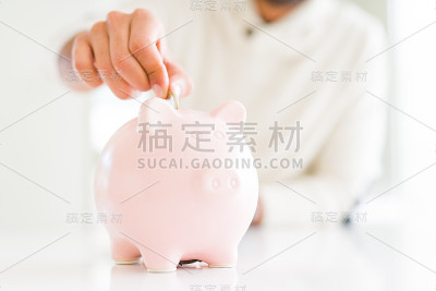 一名男子将一枚硬币放入小猪储蓄罐，为投资储蓄