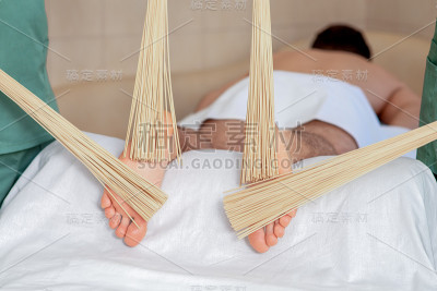 男性接受脚按摩与竹扫帚。