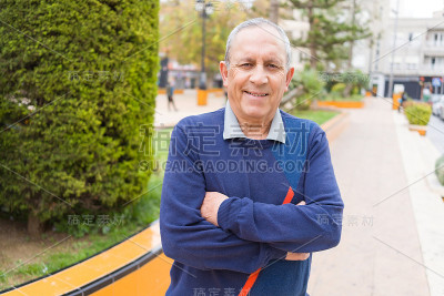 英俊的中年老人笑容开朗，幸福和积极的双臂交叉在城市城镇
