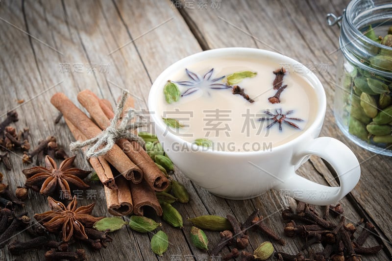 一杯健康的阿育吠陀马沙拉茶或咖啡，加牛奶和芳香香料。桌上放着肉桂棒，小豆荚，丁香和八角。