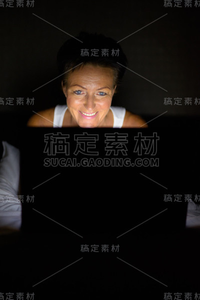 一个成熟女人晚上在酒店房间里用笔记本电脑的肖像