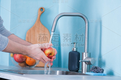 一个男人在蓝色墙壁的厨房的水槽里洗水果。以水果为背景