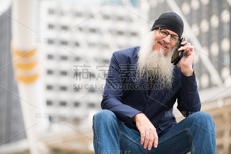 快乐成熟的大胡子商人坐在城市里打电话