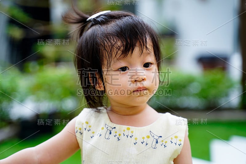 靠近可爱的亚洲女婴在户外幼儿园操场或花园。宝宝是好奇和环顾四周，孩子教育和发展学校的理念。