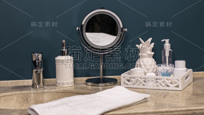 色彩新潮的浴室，洗涤区，卫生整洁。圆形金属镜，棉垫，耳棒，膏霜，液体肥皂在一个分配器。石材台面，白色