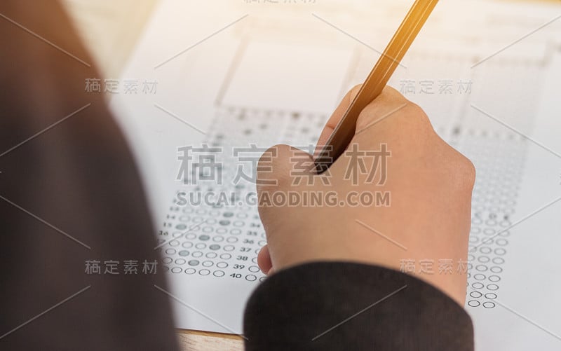 高中生或大学生手拿试卷，在答题纸上写试卷，标准化考试光学形式放在桌上，在教室里做期末考试。教育素养的