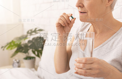 健康的老年女士在床上吃药丸，喝一杯水
