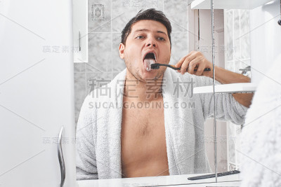 一个穿白大褂的男人用牙刷透过浴室的镜子刷他的舌头。