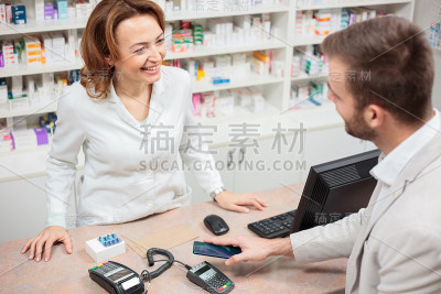 一个年轻人在药店用智能手机进行非接触支付药物的高角度视图