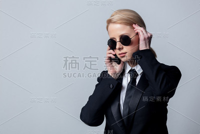 女商人穿着经典的黑色西装，戴着墨镜，正在讲手机