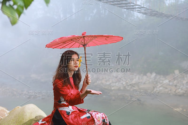 美丽的年轻亚洲妇女穿着传统的红色衣服和红色雨伞