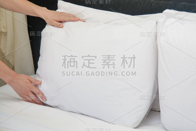 酒店客房服务。双手搭起白色枕头放在床上。