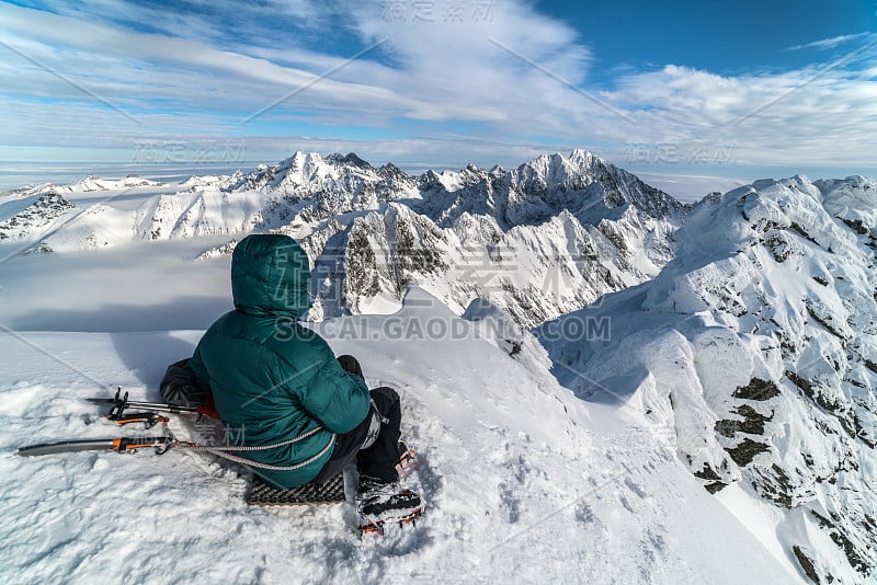 登山者坐在山顶在阳光明媚的冬日雪山