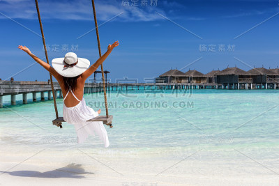 在热带海滩上荡秋千的快乐女性旅行者