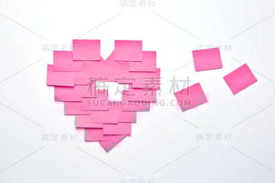 粉红色的心形便利贴贴在白色的墙上