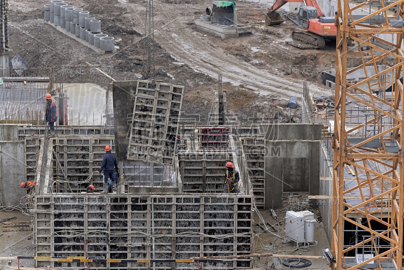 建设居民楼、沟渠和塔式起重机。一群戴着头盔和面具的建筑工在一栋在建的房子的顶层