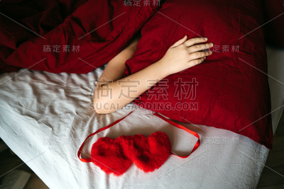 女人的手躺在一个盖着毯子的红色枕头上。女孩睡在白色的床单上