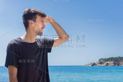 一名男子用手遮住脸挡住阳光，看着海岸