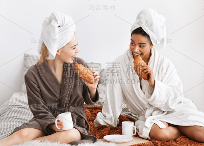 穿着浴袍的多民族女友在床上吃早餐