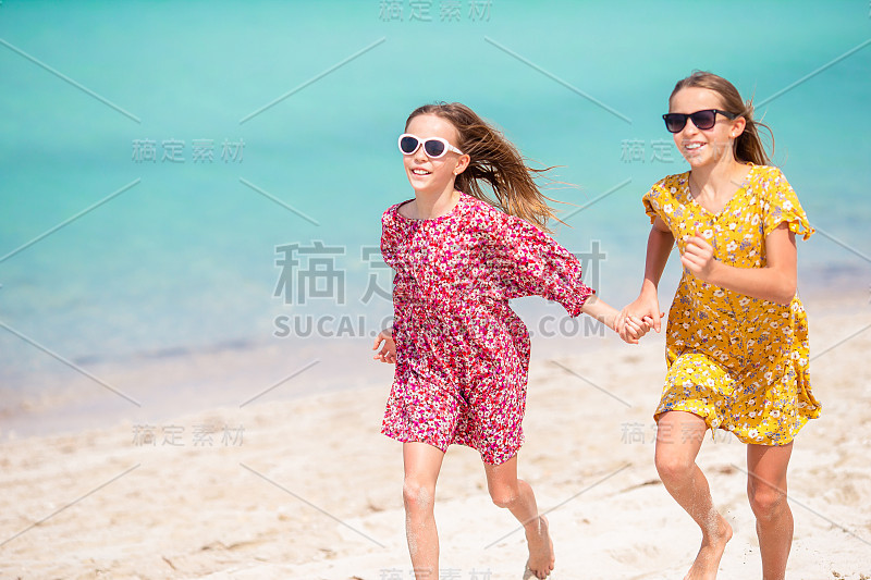 小快乐有趣的女孩有很多乐趣在热带海滩一起玩。晴天带着雨在海里