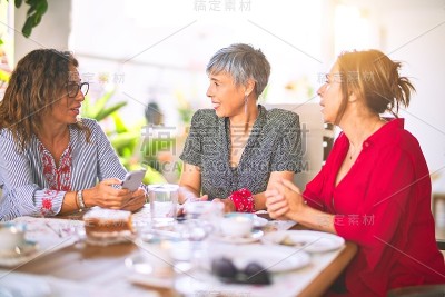 遇见中年妇女吃午饭喝咖啡。阳光明媚的日子里，成熟的朋友在家里用智能手机微笑