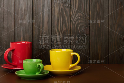不同大小和颜色的陶瓷杯咖啡和茶-红色，黄色和绿色在黑暗的木制背景。