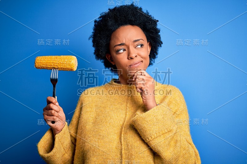 年轻的非洲裔美国素食女卷发拿着叉与玉米芯严肃的脸思考问题，非常困惑的想法