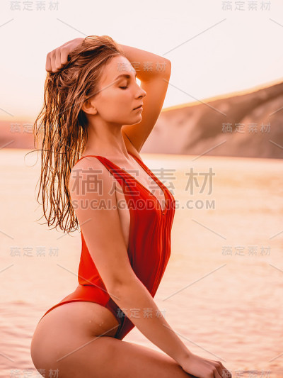 漂亮的女人在红色泳装与温暖的日落颜色在海上摆姿势。